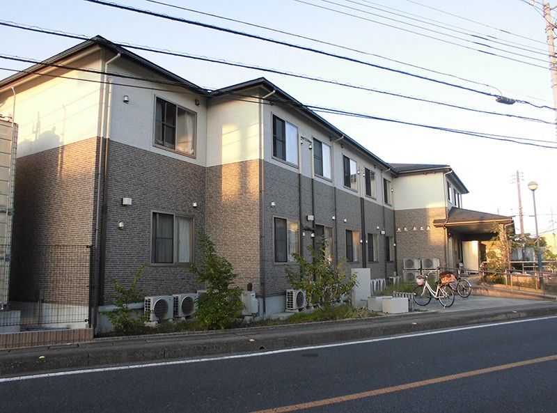 入り口にスロープがあり、茶色とベージュの外壁で三角屋根の2階建て建築物