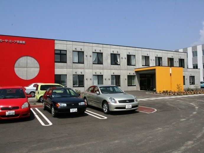 カーサ・ミーア壱番館と書かれた外壁の2階建て建築物。駐車スペースや玄関前に停まっている5台の乗用車