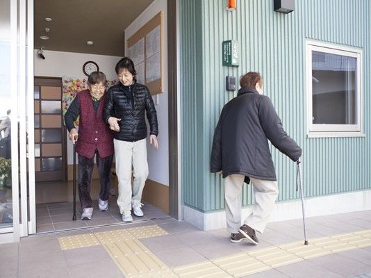 玄関の自動ドアまでは点字ブロックが敷かれ、つえを突いた入居者がスタッフと腕を組んで歩いている。