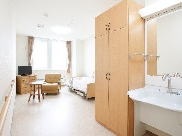 カーテンが付いた窓がある広い部屋には寝具付きのベッドやタンス、椅子、テレビがあり、車いす対応の洗面所が設置されている。