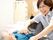 眼鏡をかけた女性スタッフが、ベッドで寝ている高齢者に対して笑顔で語りかけている。