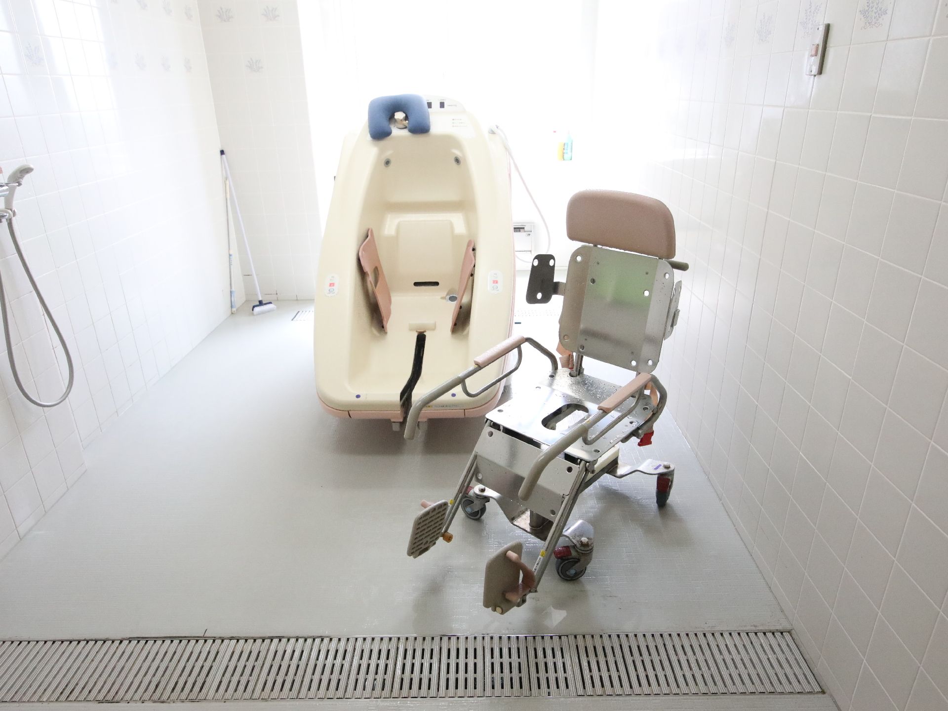 白いタイル調の部屋の中央に置かれた白い浴槽と車いす