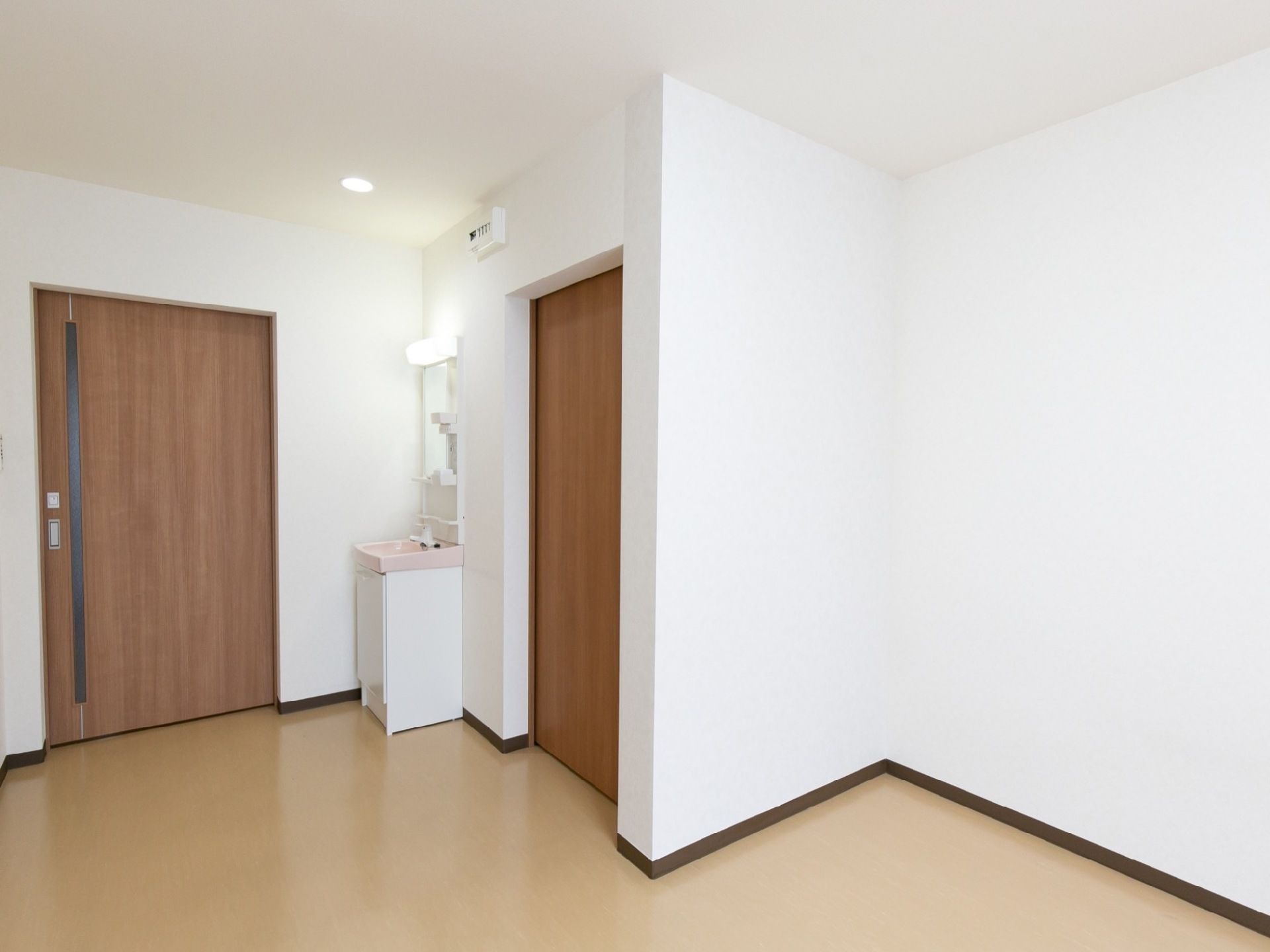 床がフローリングの洋室タイプの居室である。入口近くには洗面台が設置されており、蛍光灯や鏡が付いている。