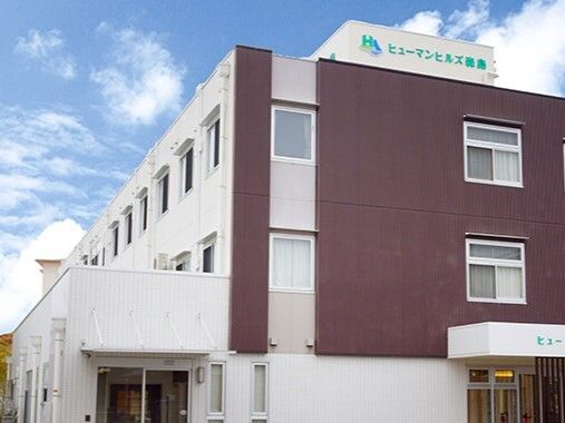 3階建ての建物はブラウンと白で、建物の一番上の部分と玄関の車寄せには住宅名が書かれている。