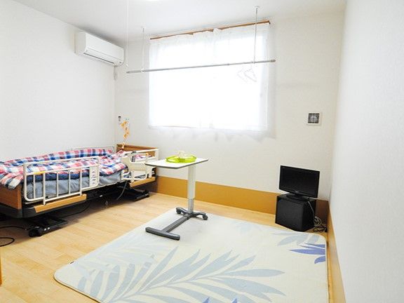 介護用ベッドやテレビがあり、床にラグが敷かれている居室