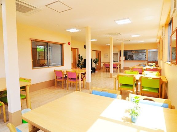 ピンクやグリーンの椅子とベージュの机が複数ある広い食堂