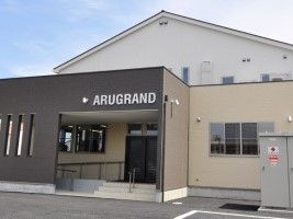 ARUGRANDと表記されている、濃茶と薄茶の外壁で三角屋根の2階建て建築物