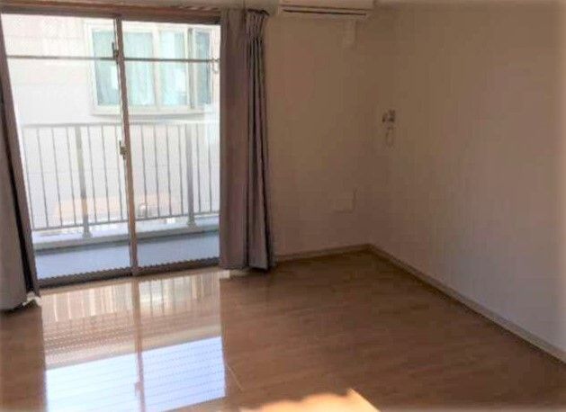 カーテン付きの大きな窓が付いたシンプルな居室には家具はなく、テラスやエアコンがある。