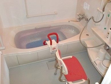 シャワーチェアが設置された浴室にはたくさんの手すりが設置され、シャワーや洗面器も付いている。