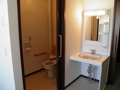 引き戸が付いたトイレは手すりや背もたれが付き、洗面所は車いす対応のデザイン。白い壁で清潔感がある。