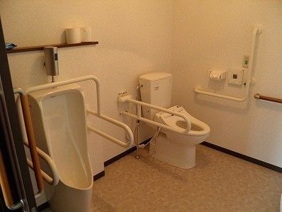 エル字型の手すりや呼び出しボタンが洋式トイレの横につき、男性向けのトイレにも手すりが設置されている。
