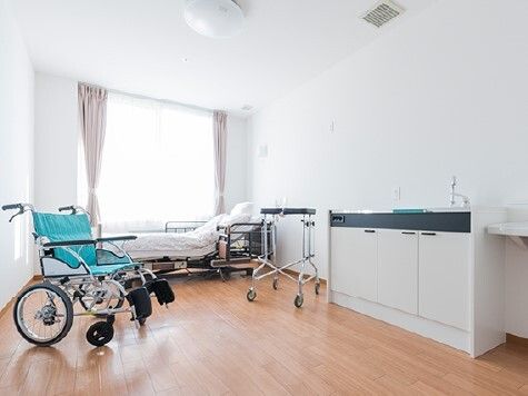 大きな窓が付いたフローリングの部屋には介護ベッドやキッチンがあり、車いすや歩行器も置かれている。