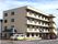 4階建てのベージュを基調とした建物の前には施設の車が二台並び、屋外の階段も設置されている。