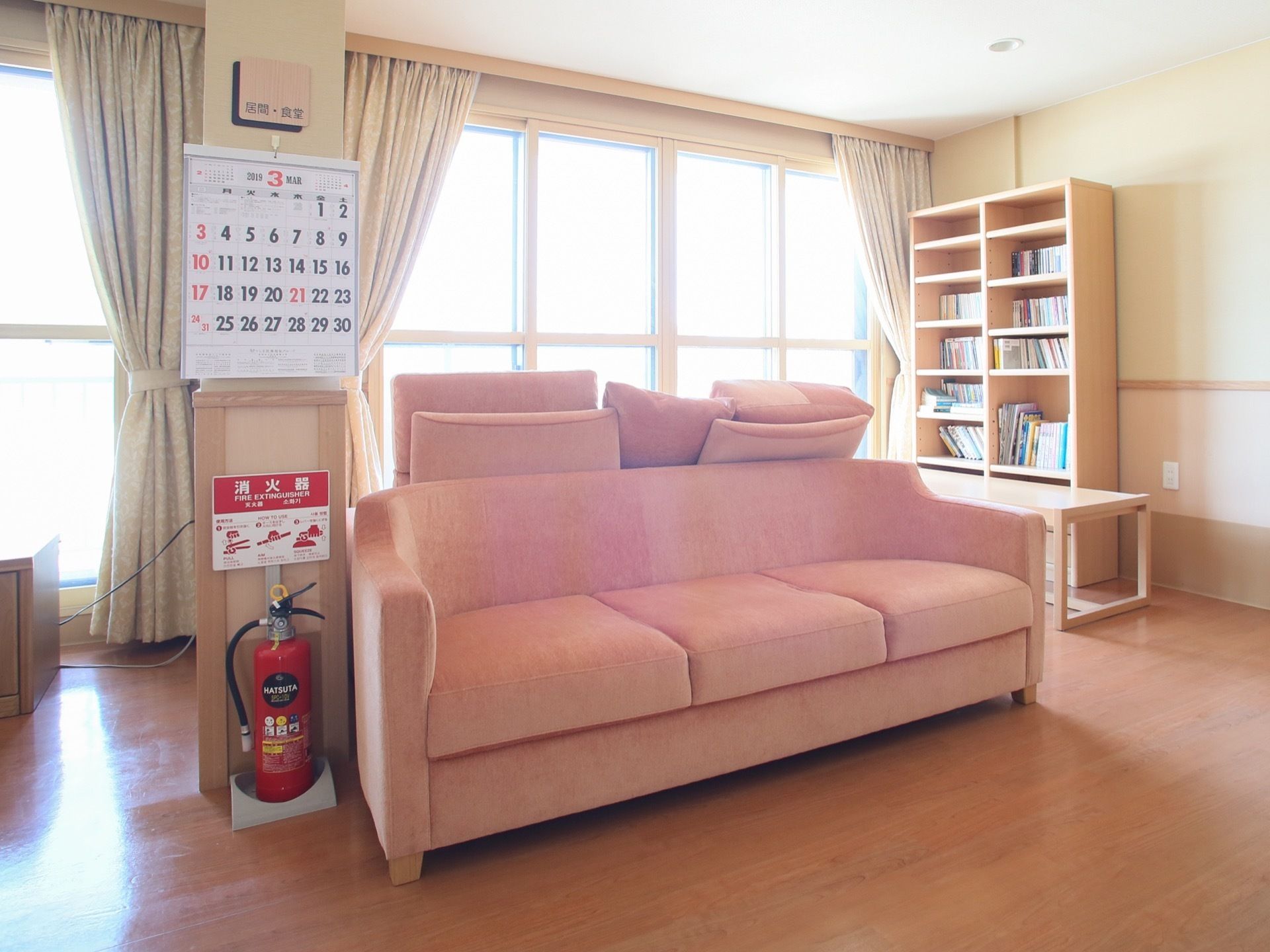 窓の前に、ふかふかのピンク色のソファが置いてある。その近くには本棚があり、多くの本が収納されている。