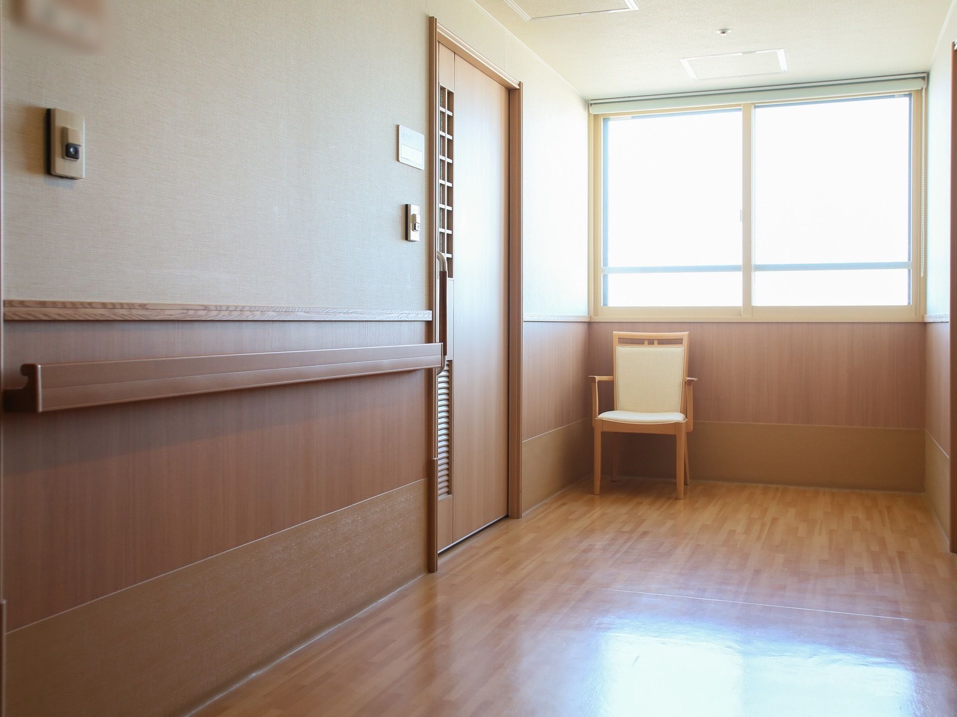 ベージュの壁紙で壁の下半分と床は木目で、温かみのある廊下である。居室のドアには、手すりの他にも格子状の小窓が取り付けられている。