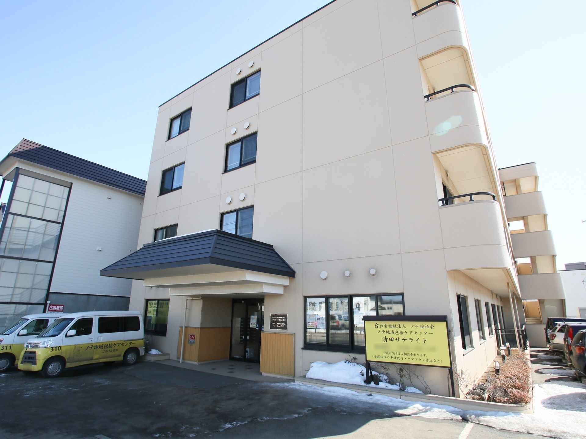 ベージュを基調とした4階建ての建物には駐車スペースもあり、玄関先には屋根が付いている。