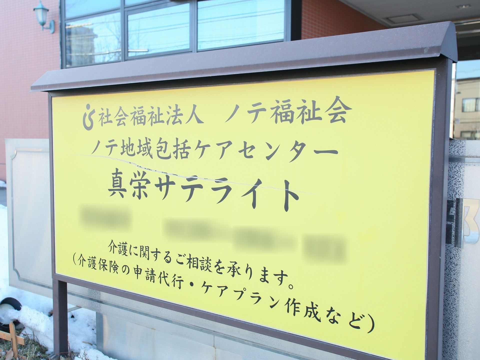 施設の外に設置されている、黒いフレームに囲まれた看板がある。黄色い板面には施設名とメッセージが書かれている。
