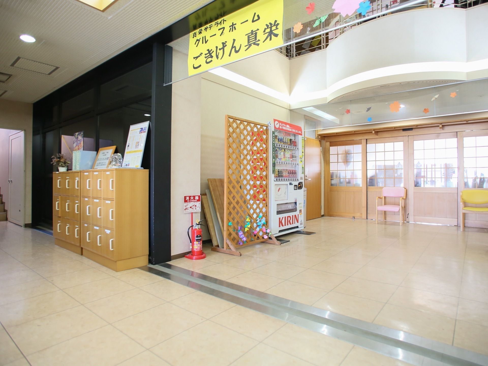 一部が吹き抜けになっている玄関ホール。下駄箱と自動販売機が置かれている。天井付近には施設名が書かれた色紙と、手作りの飾りつけがされている。