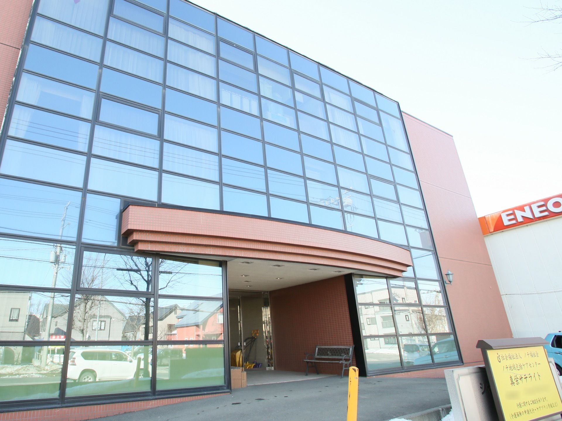 前面部分が一面ガラス張りになっている大きな建物がある。玄関部分にはルーフが付いており、地面は緩くスロープになっている。