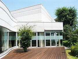 白い建物は広いウッドデッキや庭が付き、おしゃれな雰囲気。共有スペースはガラス張りで明るい。