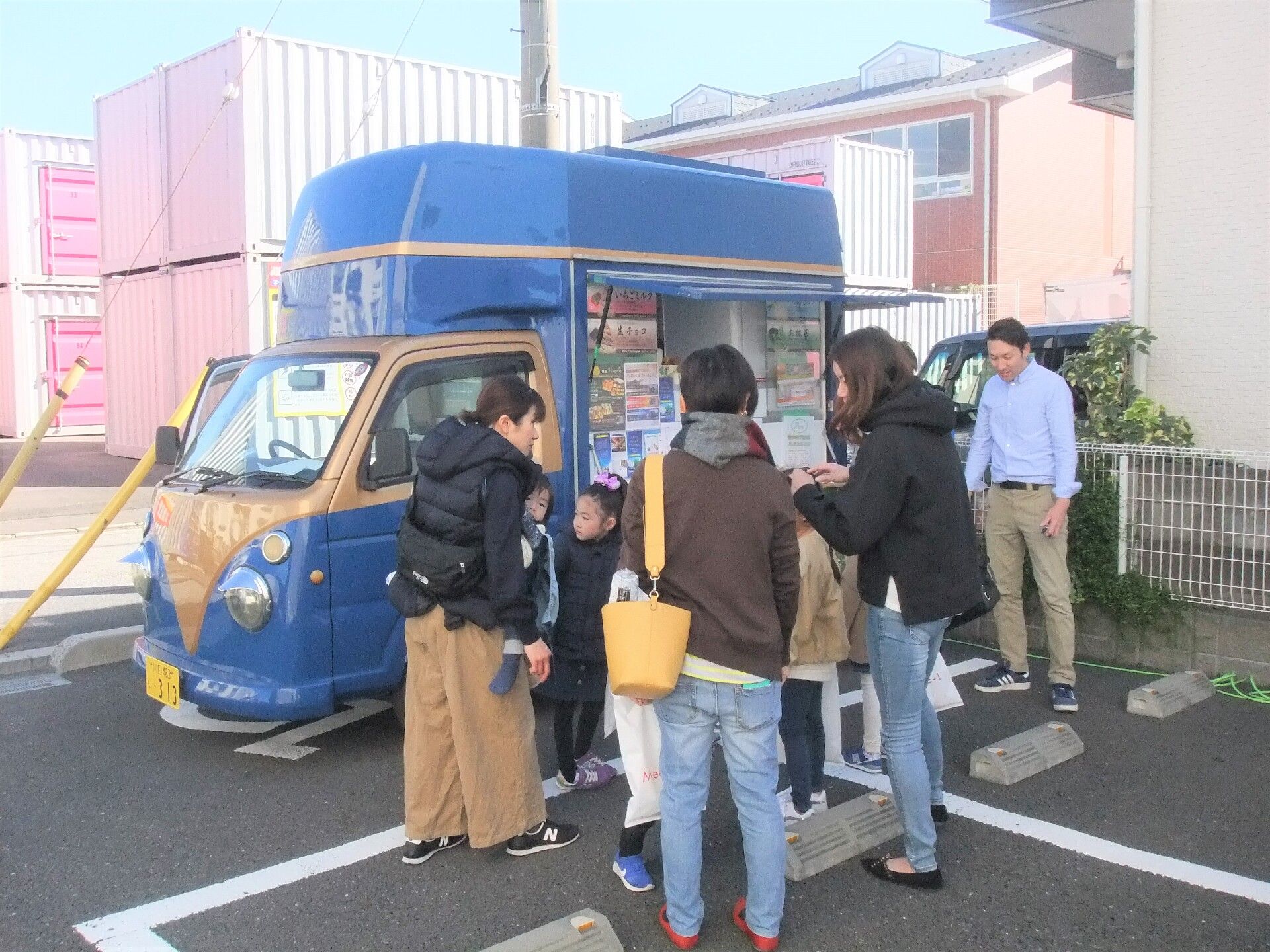 ピンクのエプロンを付けた女性スタッフが車いすの高齢女性と一緒に日当たりのいい屋外を散歩している様子。