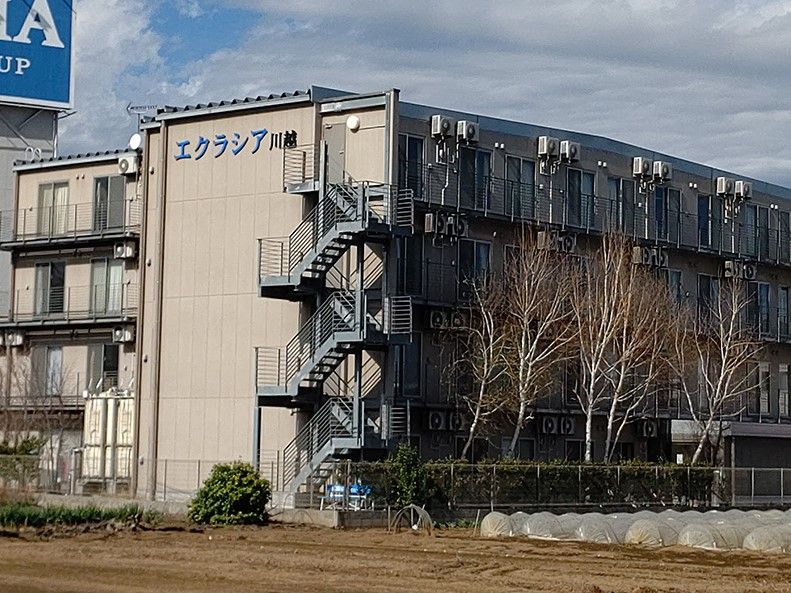 緑に囲まれた敷地内にあり、エクラシア川越と書かれている4階建て建築物