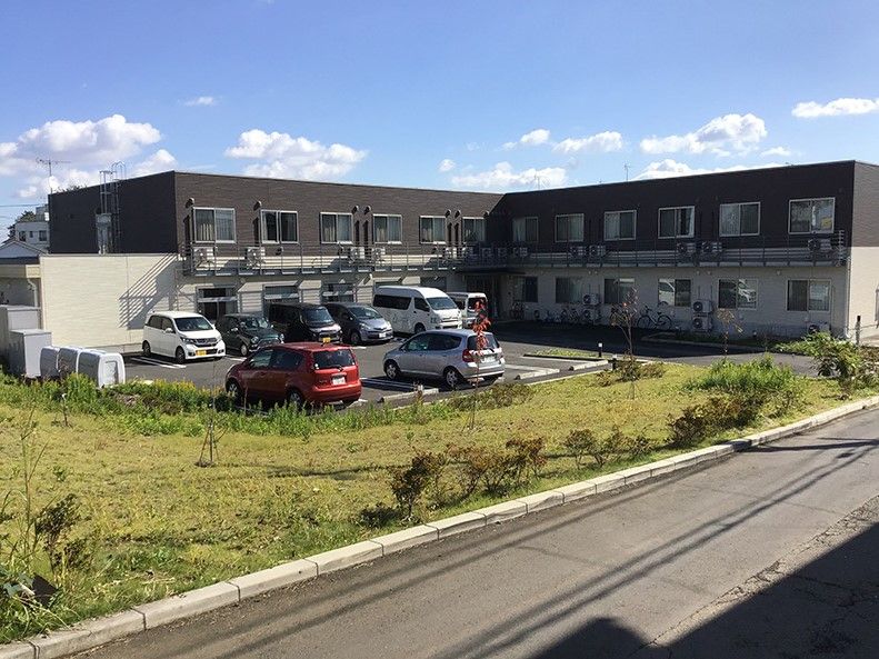 周りが緑に囲まれている茶色とベージュの外壁の2階建て建築物