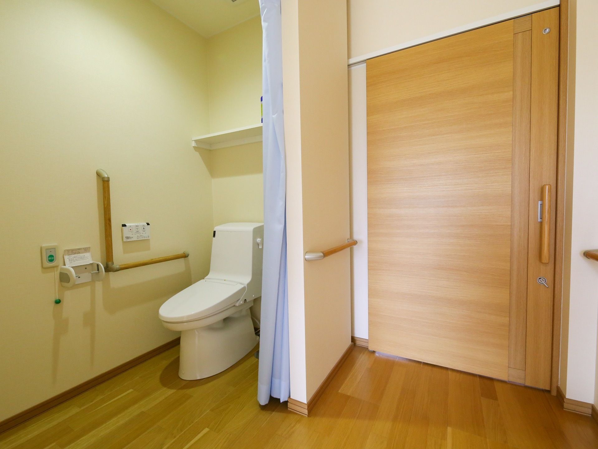 温水洗浄便座のトイレが設置されている。壁にはL字型の手すりが備わっており、緊急呼び出しボタンが取り付けられている。