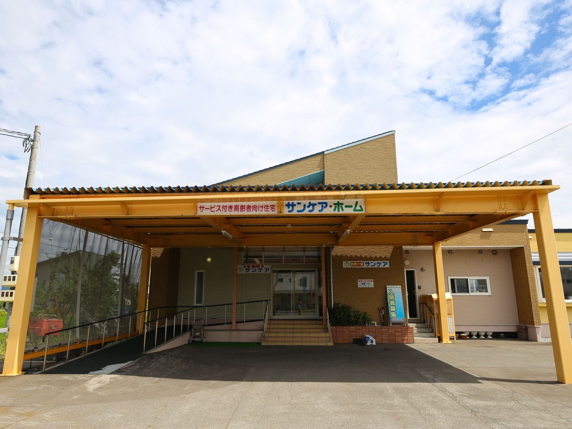 屋根を設けたエントランスポーチが完備された施設入口である。左サイドには、手すり付きのスロープが設置されている。