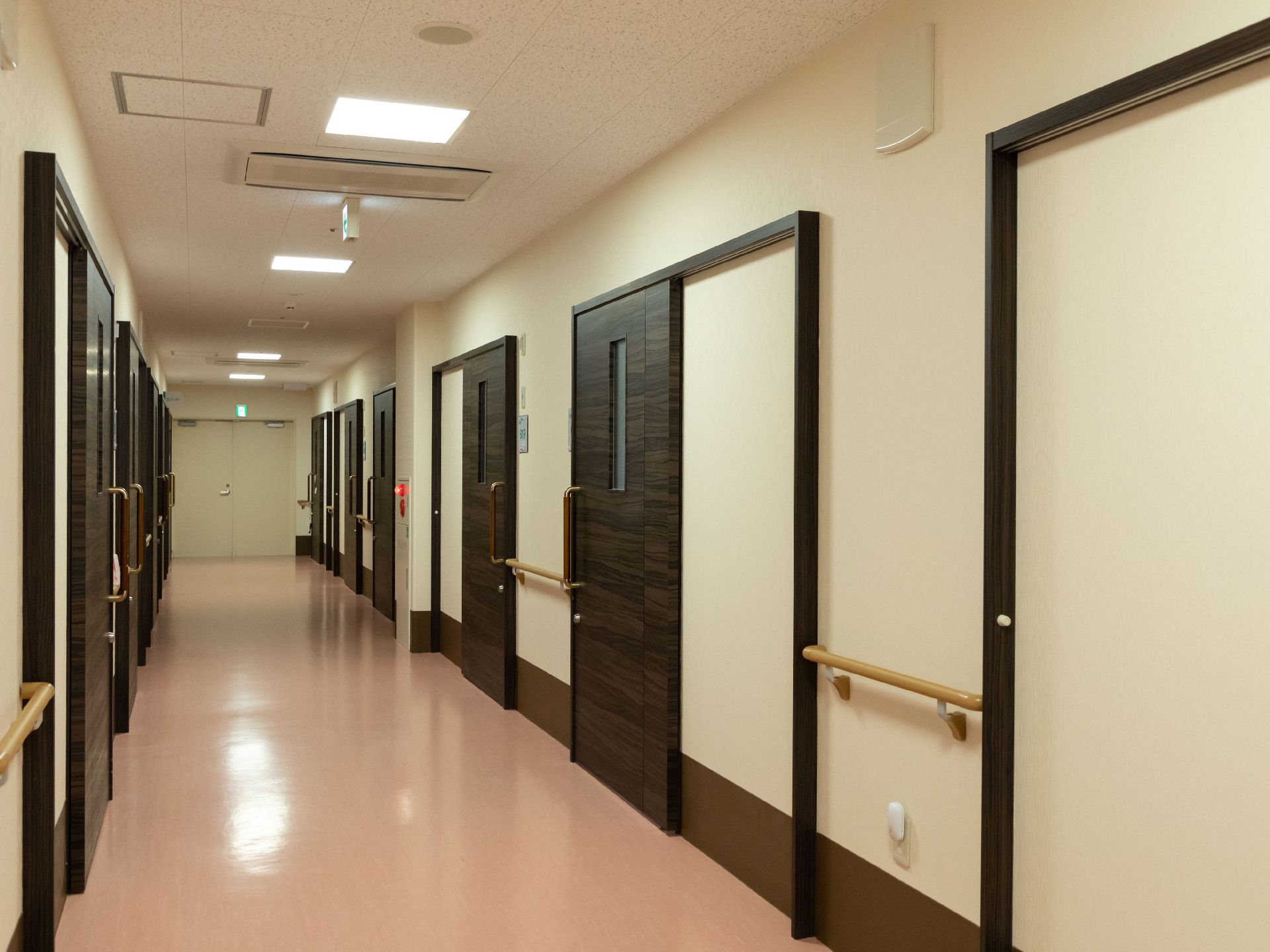 両側の白い壁に木製の手すりと扉が配置された直線の廊下