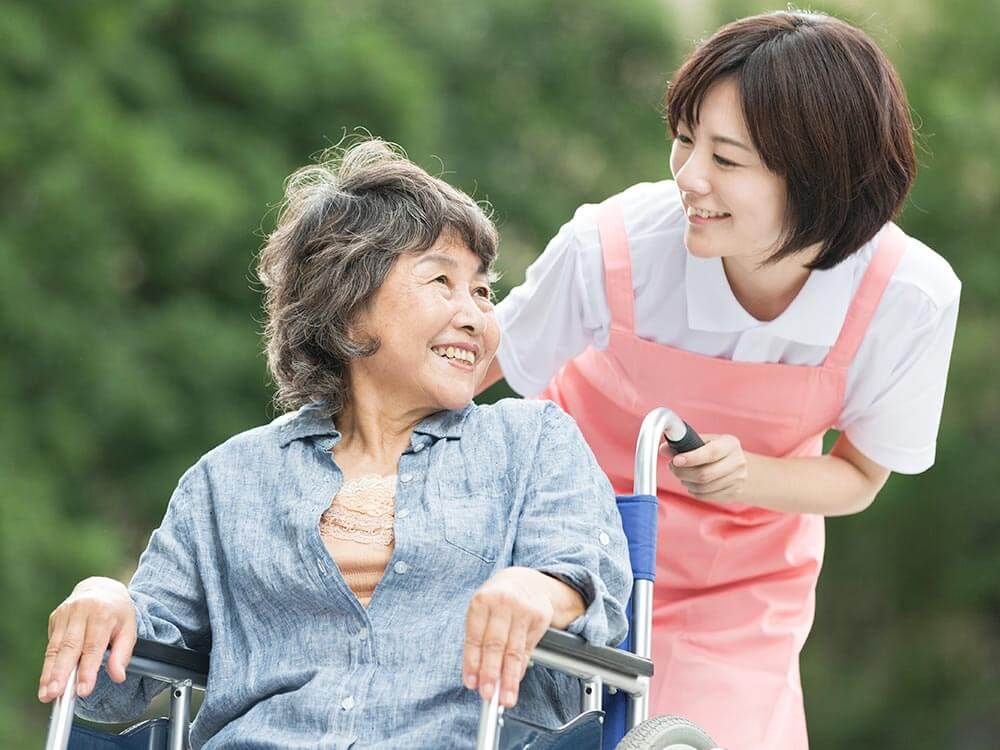 車椅子に乗った高齢女性と付き添いの女性ヘルパー