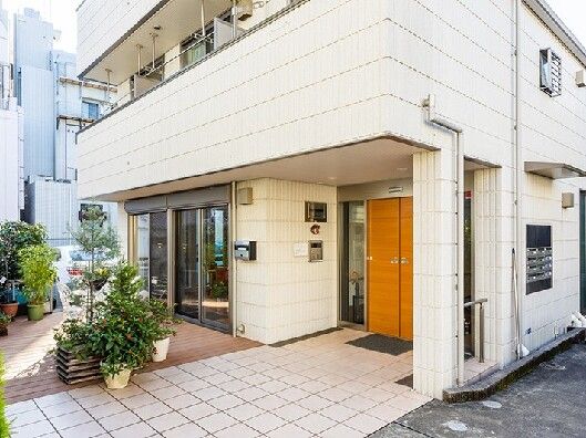 インターホンが玄関に付き、段差のない白い建物。周りには草木が植えられた鉢がたくさんある。