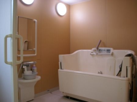 リフト浴が設置された浴室内には洗面器やシャンプーなどもあり、壁には手すりが付き、シャワーもある。