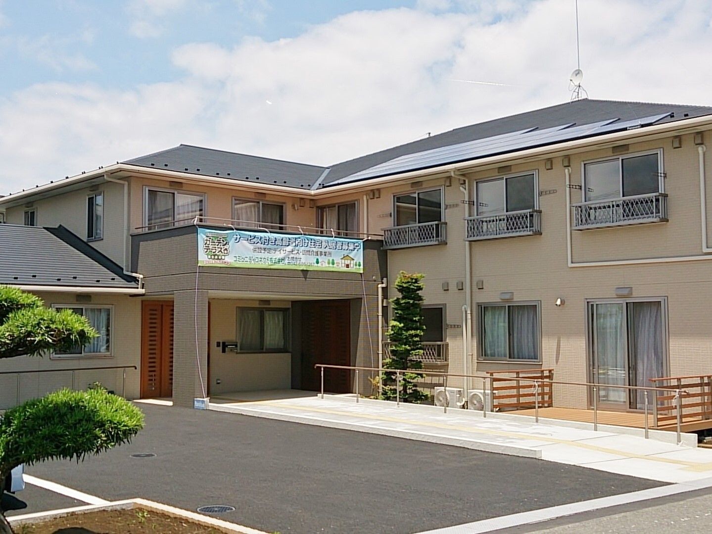 グレーの屋根が付いたべ－ジュの２階建ての建物はエル字型で、駐車場も完備されている。