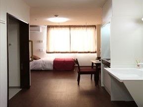 日の光が差し込んでいる広めの部屋。手前に洗面台、奥のほうにベッド