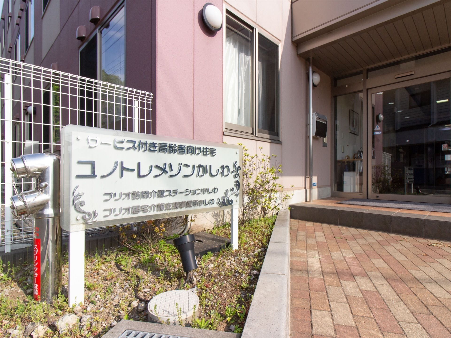 玄関前の花壇に、横長の看板が設置されている。提供サービス形態と施設名称が大きな文字で表示されている。