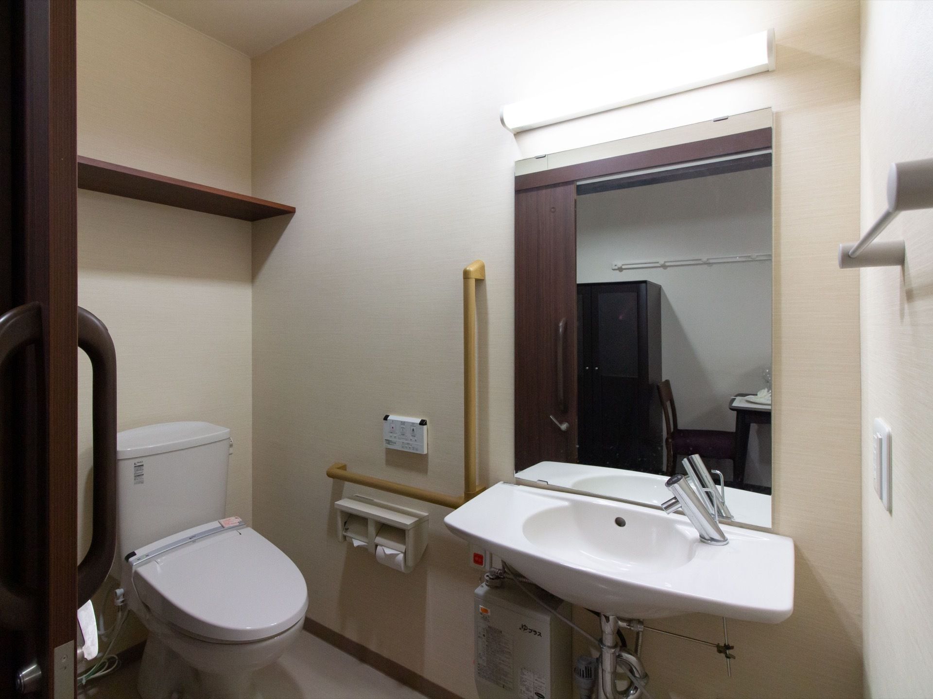 居室のトイレは、大きな取っ手がついた引き戸を開けた所に設置されている。大きな鏡がついた洗面台もある。