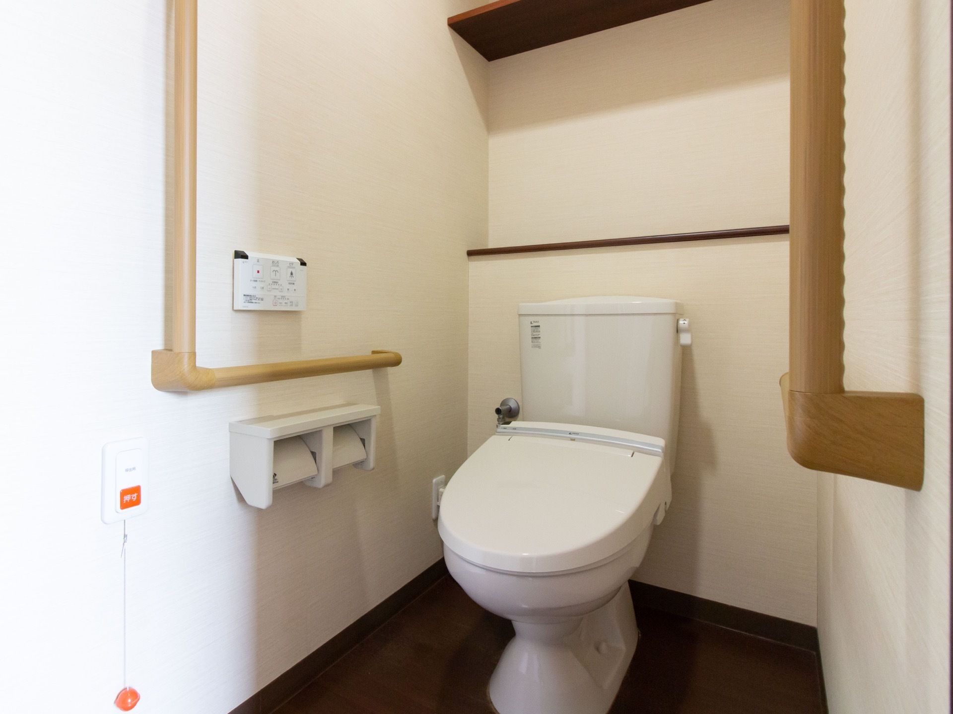 トイレは、ふたつきの便座になっている。トイレットペーパーホルダーが２つ並んで設置されている。大きな手すりがある。