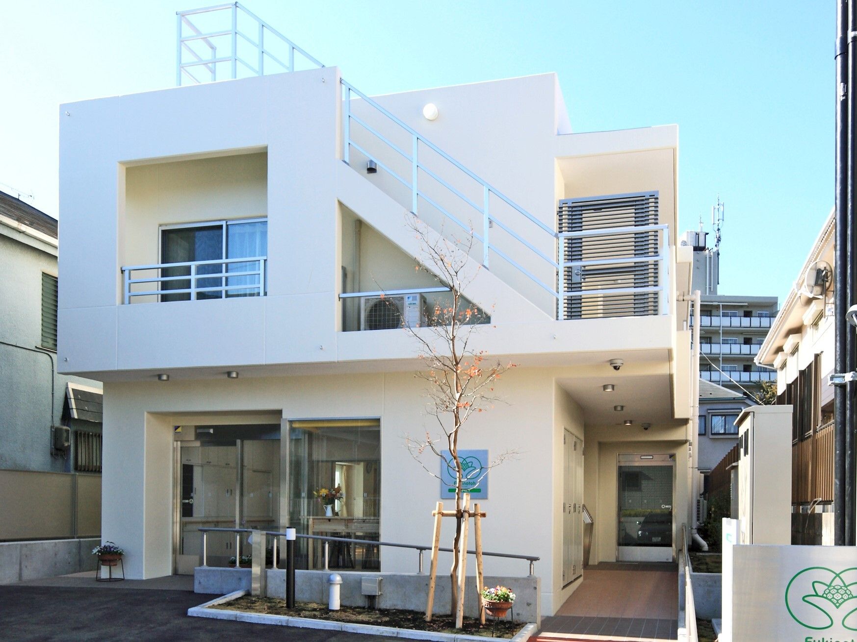 白を基調とした２階建ての建物。敷地内には草木が植えられ、屋外階段やベランダもあり、玄関はオートロック。