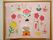 白壁に茶色の額縁でひな祭りと書かれた装飾品が飾られている。お雛様やひなあれなどを形どった絵や折り紙を貼り合わせた可愛らしい制作物。