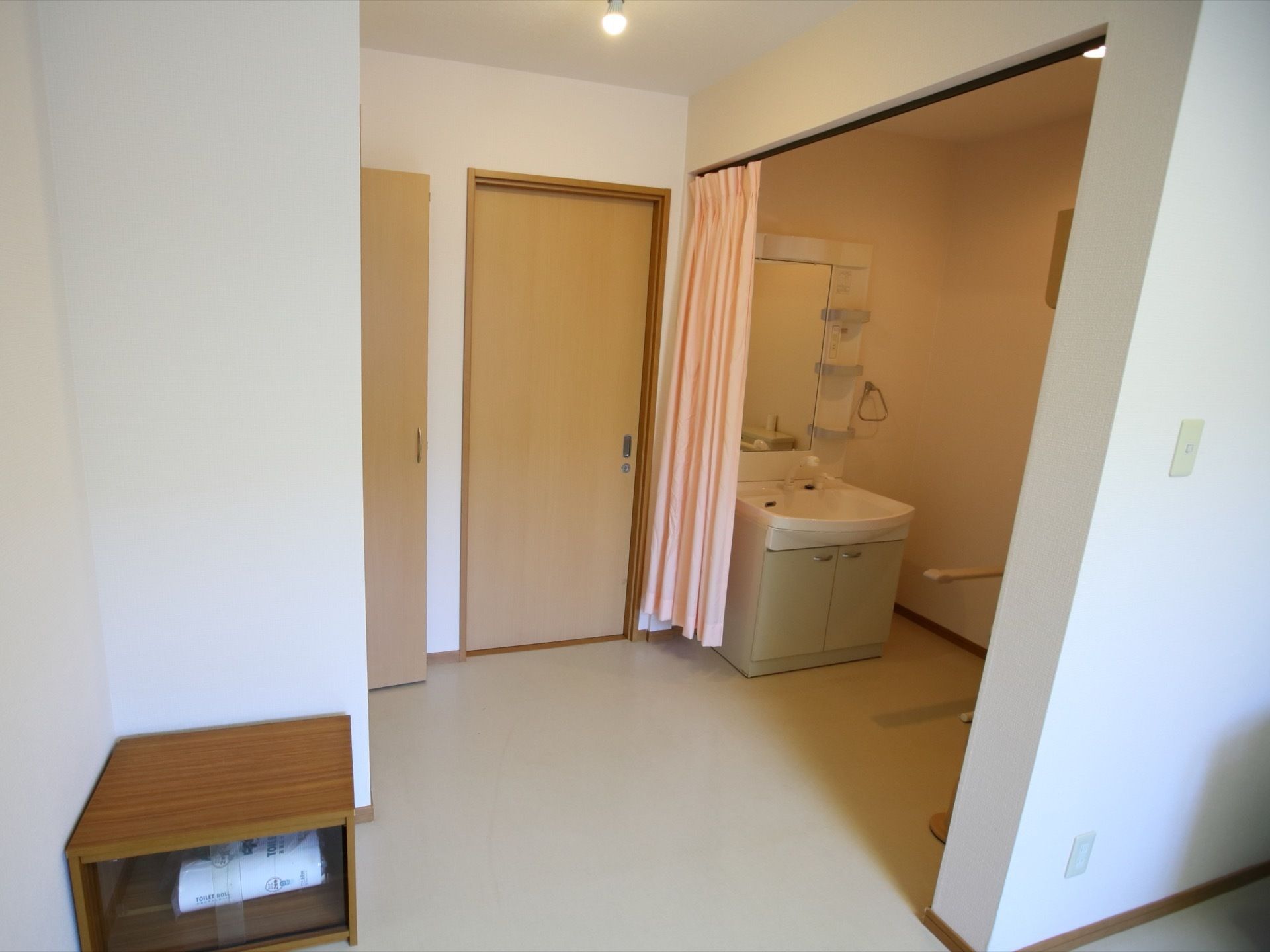 居室扉のそばには、洗面化粧台とトイレが同スペースに設置されている。通路との仕切りにカーテンが引かれている。