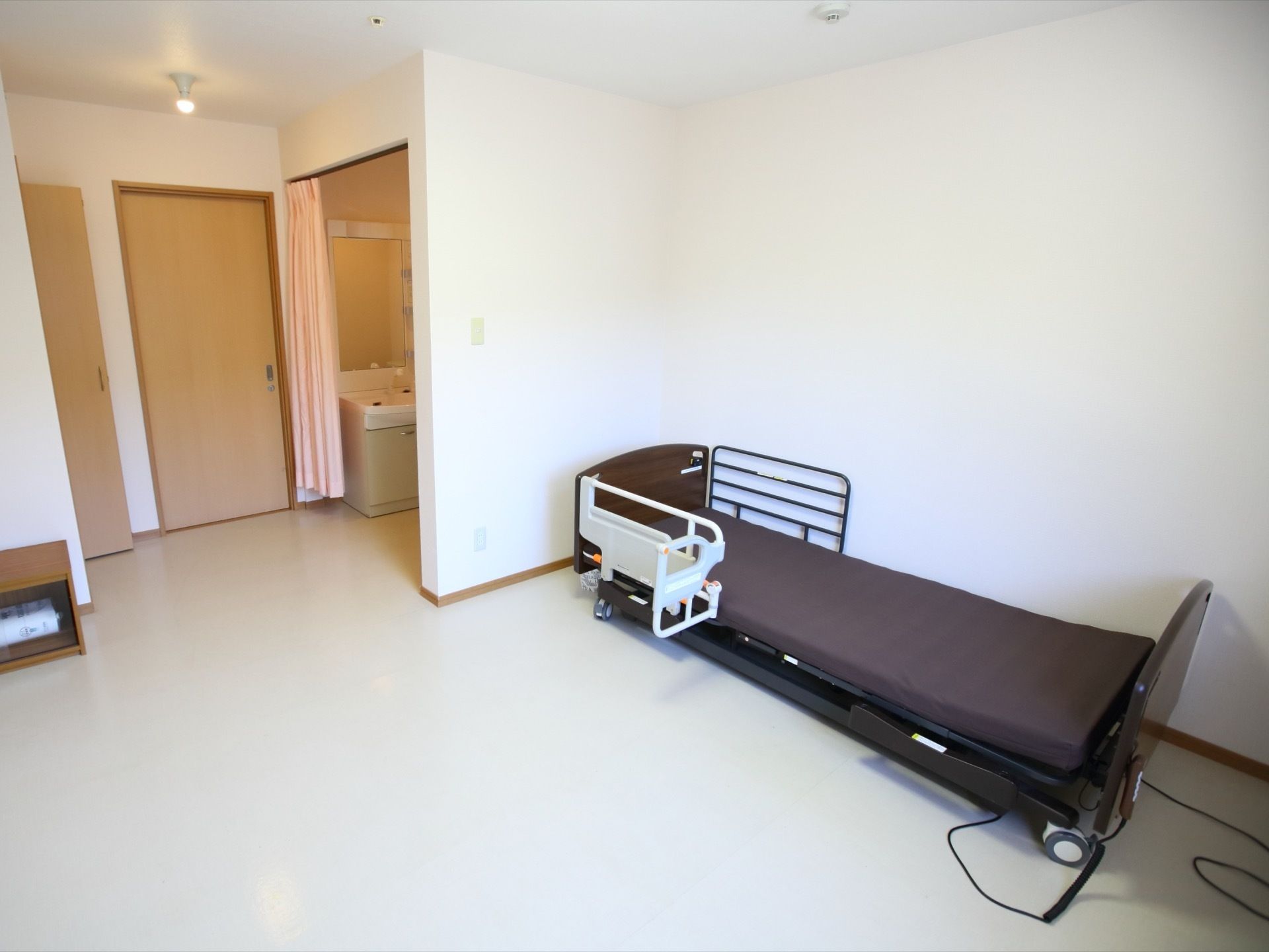 居室の白い壁際に未使用の介護用ベッドが設置されている。リモコン操作でリクライニングや昇降が自由にできる。