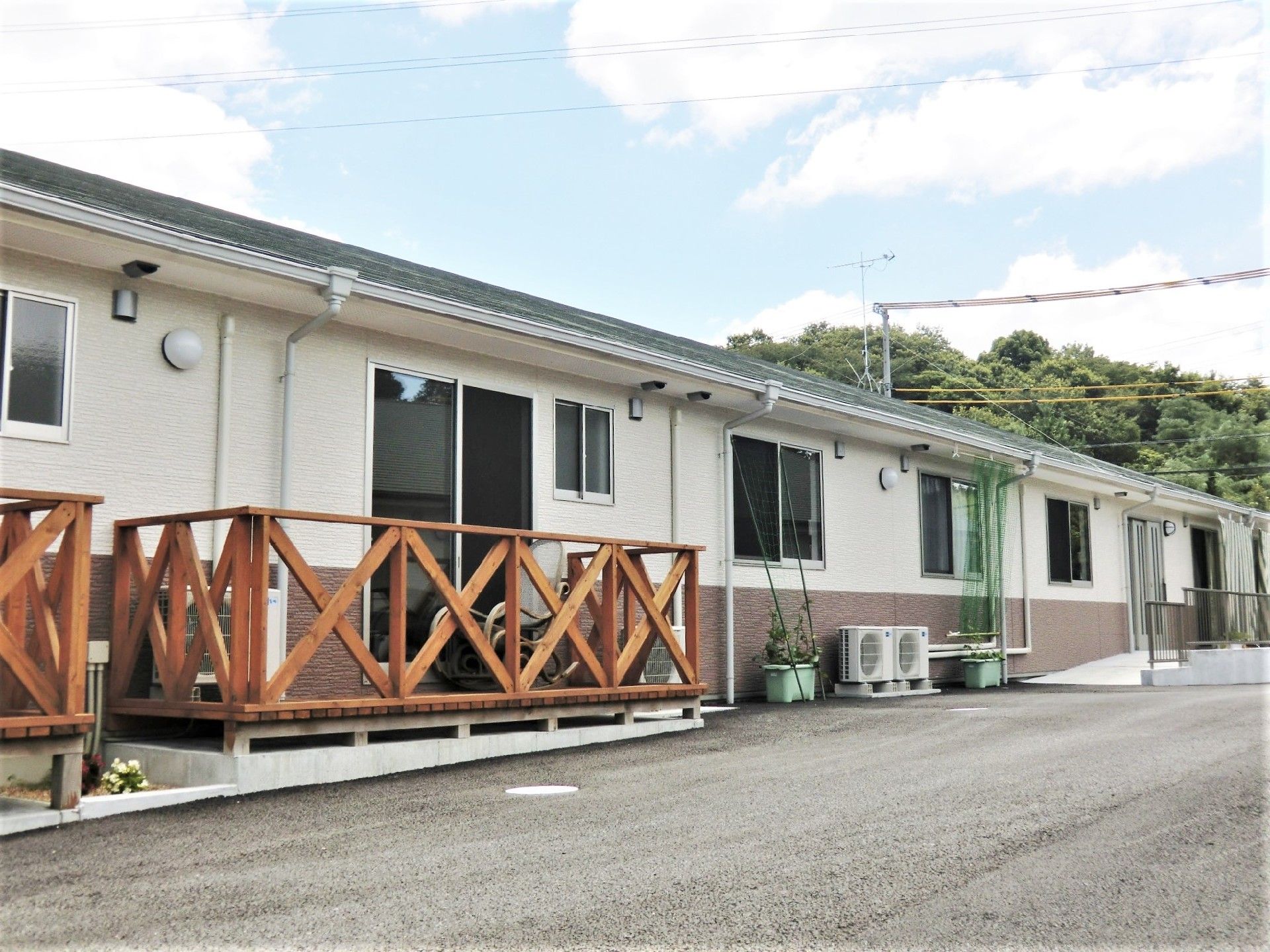 ウッドデッキのベランダが付いた平屋建ての建物。周辺には緑が多い。