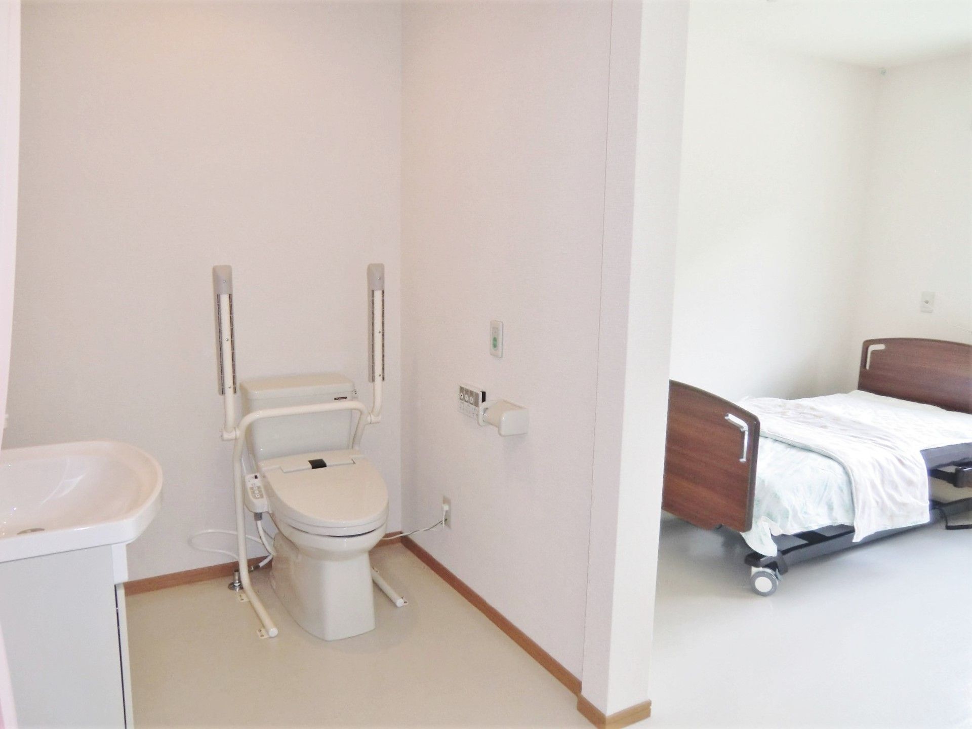 右手にはベッド、左手には洗面所とトイレがあり、トイレには可動式の手すりが設置されている。