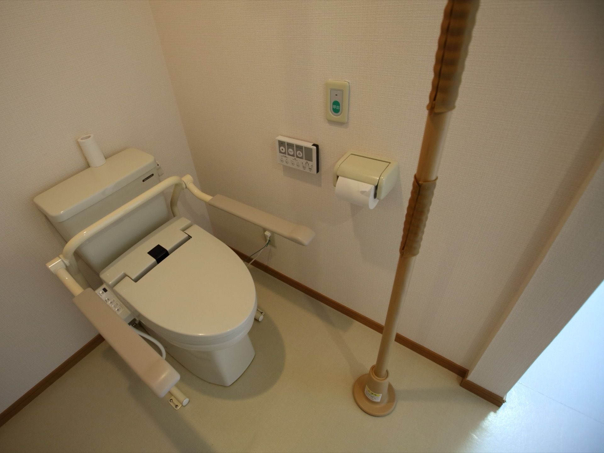 温水洗浄機能付きのトイレである。壁にはナースコールや操作パネル、ペーパーホルダーが取り付けられている。