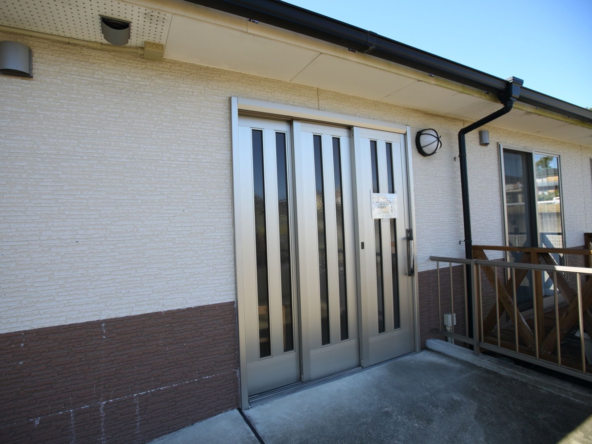 平屋建ての建物で、白を基調とした外壁には照明が設置されている。玄関横の部屋には、ベランダが設けられている。