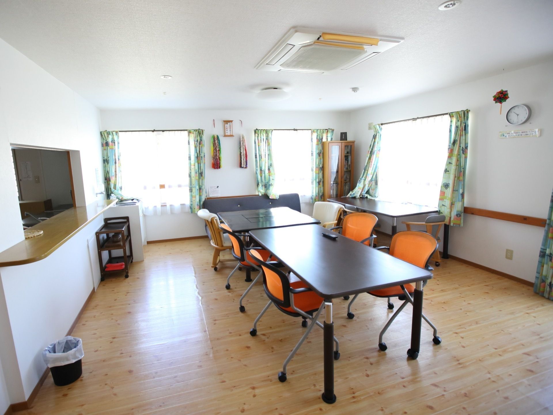 空調設備が整っている明るい食堂で、窓にはデザイン性のあるカーテンが取り付けられている。フロア隅には、本棚が置かれている。