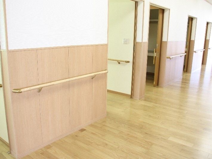手すりが設置されたまっすぐな廊下。日当たりもよく、居室には大きなスライド式のドアが付き、フロアには余計なものは置かれていない。