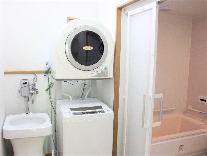 ピンクの浴室には一人用の浴槽が付き、脱衣所には縦型の洗濯機と乾燥機、手洗い専用のきれいに掃除がされている。