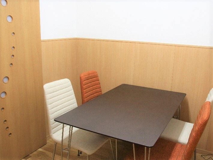 赤と白の椅子が2脚ずつセットされたダークブラウンのテーブル。部屋の中にその他のものはなく、ドアには大小の丸い小さな光窓がある。